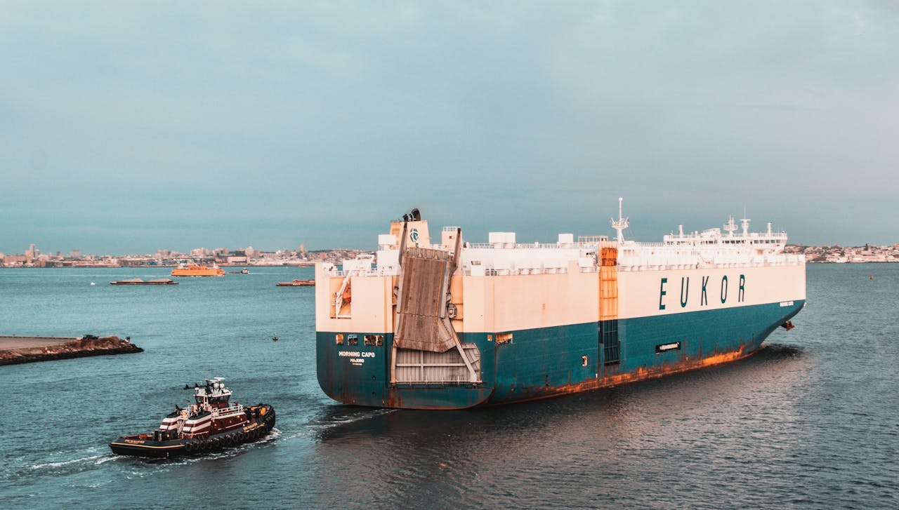 A cargo ship navigates a harbor, assisted by a tugboat, under a clear sky.