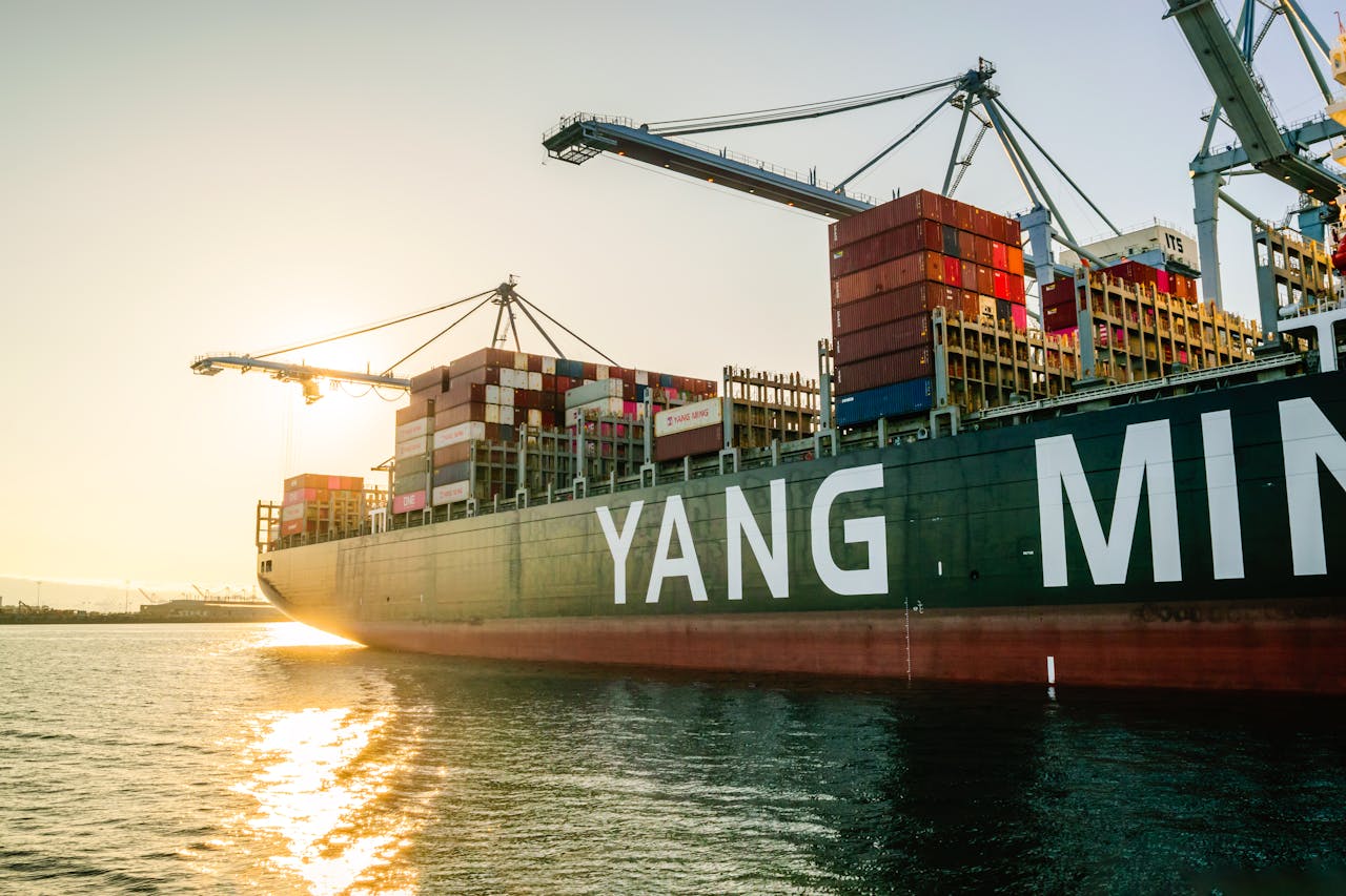 services-05 Large cargo ship with stacked containers and cranes at sunset in a harbor.