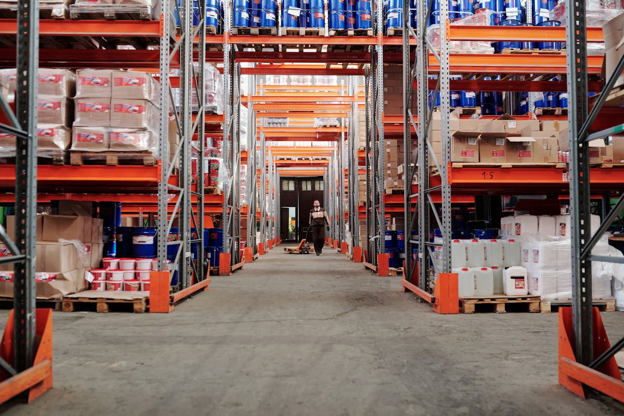 A spacious industrial warehouse with stocked shelves and a worker in protective gear.